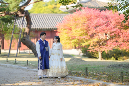 A Korean couple in their 30s and a woman in their 20s are happily wearing Hanbok and spending time in front of beautiful autumn leaves in a historical building in Seoul, South Korea.の写真素材