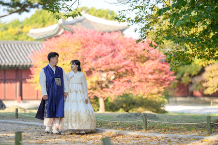A Korean couple in their 30s and a woman in their 20s are happily wearing Hanbok and spending time in front of beautiful autumn leaves in a historical building in Seoul, South Korea.の写真素材