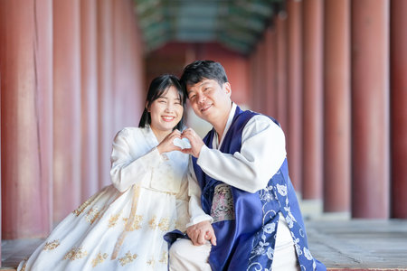 A Korean couple, a man in his 30s and a woman in her 20s, are happily wearing Hanbok and sitting in a historical building in Seoul, South Korea.の写真素材