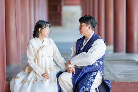 A Korean couple, a man in his 30s and a woman in her 20s, are happily wearing Hanbok and sitting in a historical building in Seoul, South Korea.の写真素材