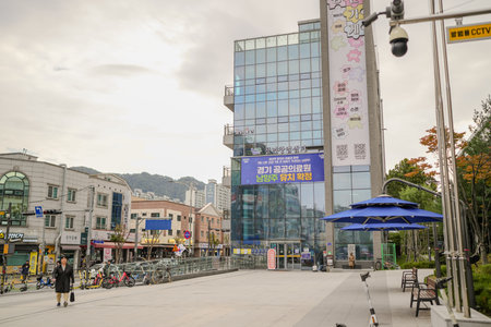 City street with a large building in the background. There are several people walking around and a few parked carsのeditorial素材