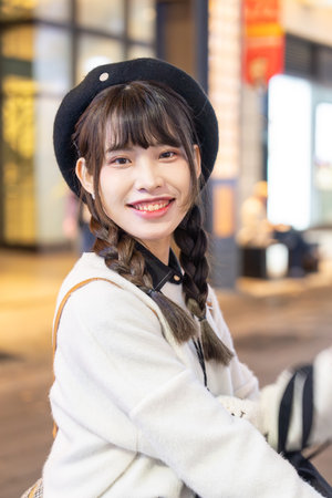 A young and cute Taiwanese woman in her 20s wearing black and white clothes, sitting and resting at night amidst beautiful illuminations in a shopping mall in Xinyi District, Taipei, Taiwanの写真素材