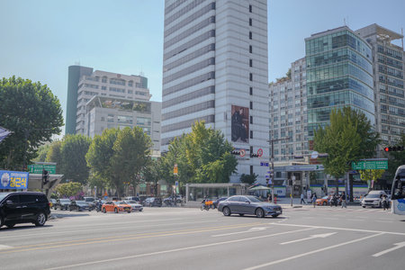Busy city street with a large white building in the background. There are many cars on the street, including a silver car and a black car. A bus is also on the streetのeditorial素材