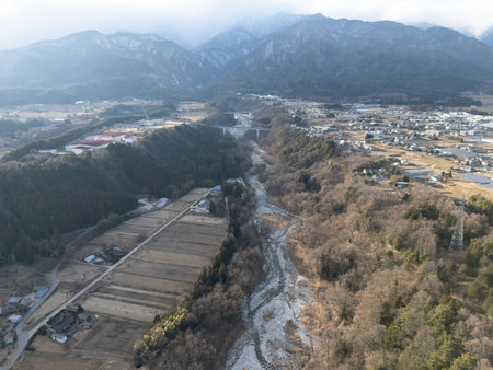 Aerial photograph of the countryside, including rice and private houses, including snow-covered Mt. Senjogatake and Mt. Kiso-Komagatake in Komagane City, Nagano Prefecture, Japan in winter.の写真素材