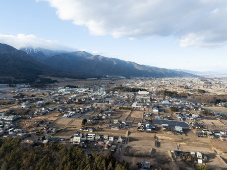 Aerial photograph of the countryside, including rice and private houses, including snow-covered Mt. Senjogatake and Mt. Kiso-Komagatake in Komagane City, Nagano Prefecture, Japan in winter.の写真素材