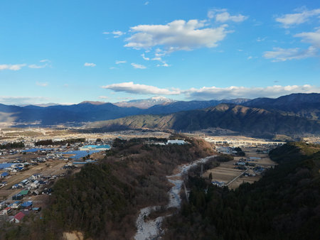 Aerial photograph of the countryside, including rice and private houses, including snow-covered Mt. Senjogatake and Mt. Kiso-Komagatake in Komagane City, Nagano Prefecture, Japan in winter.の写真素材