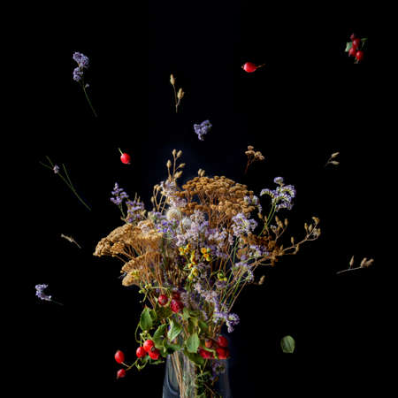 Beautiful autumn bouquet composition of dried meadow flowers with leaves, floral on black background. Floristic art decoration closeup, top view with copy space.の写真素材