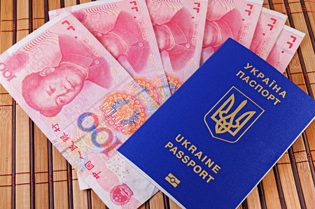 Ukrainian passport and yuans closeup on background of bamboo matの写真素材
