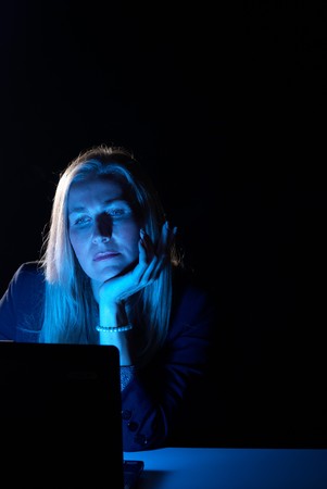 Blue computer screen reflecting on late working businesswomanの写真素材