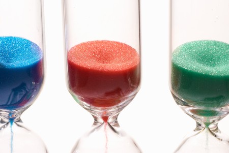 Multicolored sand pouring down several hourglasses, time is tickingの写真素材