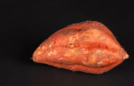 A raw sweet potato isolated on blackの写真素材