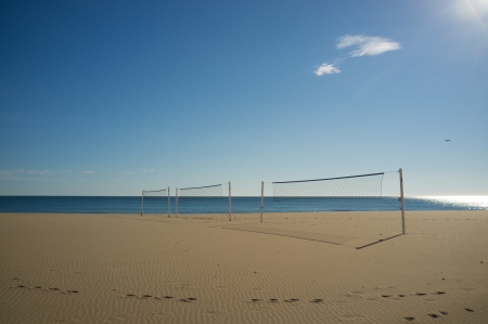 Beach volley nets on a sunny Mediterranean beach resort,  with an  jetliner approaching to a nearby airportの写真素材