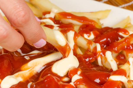 Female hands dunking fries in ketchup and mayonnaise