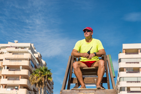 Lifeguard sitting high up on his chair watching the beachの写真素材