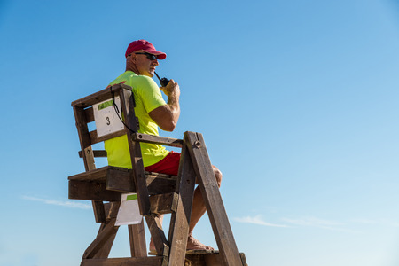 Lifeguard sitting high up on his chair watching the beachの写真素材
