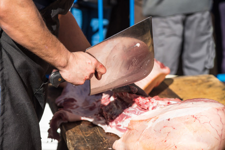 Butcher working outdoors preparing a pork leg to become ham during a traditional festiva