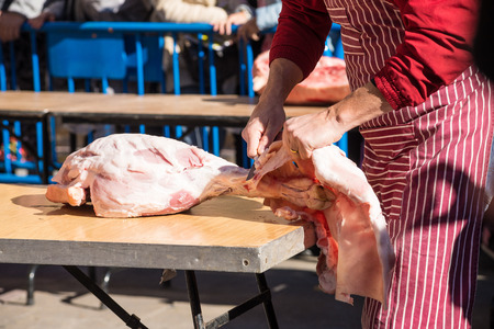 Butcher working outdoors preparing a pork leg to become ham during a traditional festiva
