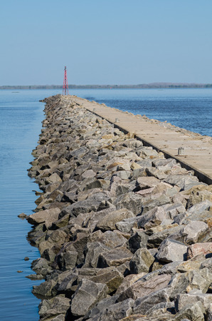 Large rock breakwater with a red beacon on its tipの写真素材