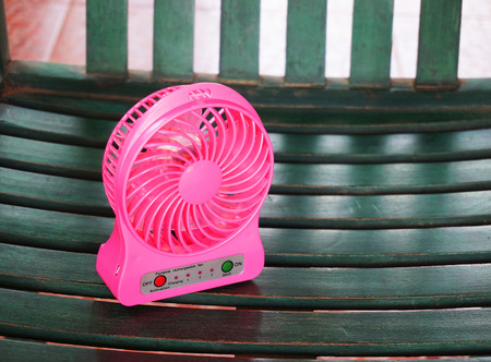 Pink  portable Fan USB  on the green wooden chair.の写真素材