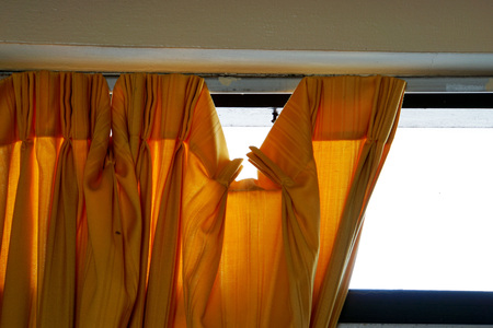 Old orange curtain falls off the track with transparent glass that reflect light in sunny day is behind the scene.の写真素材