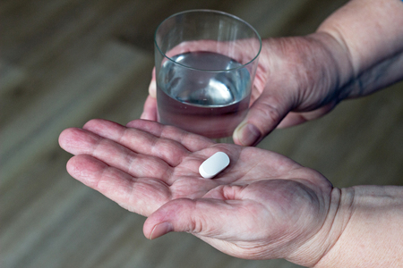 Tablet in hand and glass of water, elderly woman, close-upの写真素材