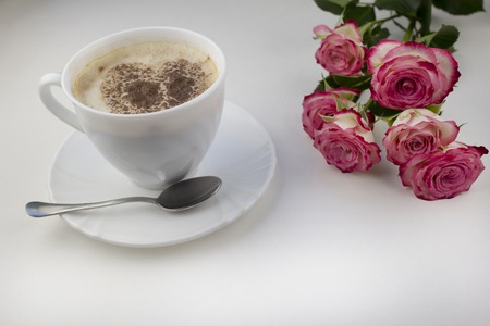 Coffee with foam with a heart of cinnamon on a white background. pink rosesの写真素材