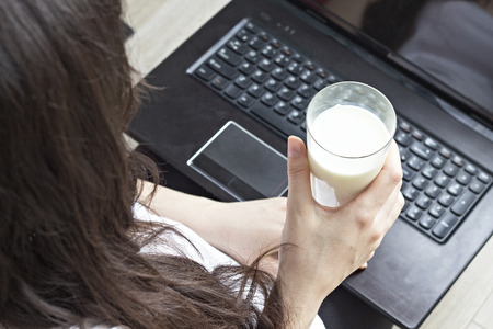 Brunette girl holding milk in a glass, laptop, healthy food, close-upの写真素材