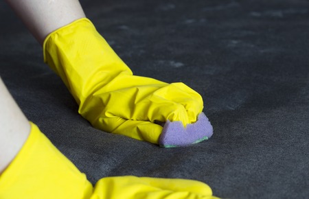 girl in yellow gloves cleans the sofa, close-upの写真素材