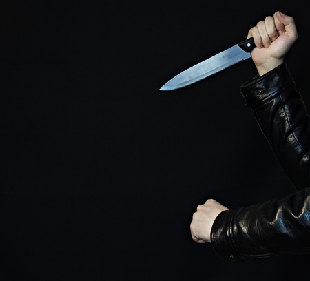 Male hands with a knife and fist on a black background, close-up