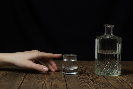 female hand reaches for a glass with alcohol, black backgroundの写真素材