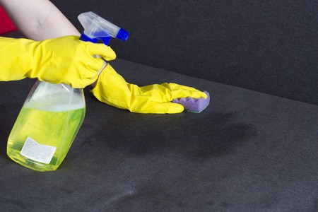 girl in yellow gloves cleans the sofa, close-upの写真素材