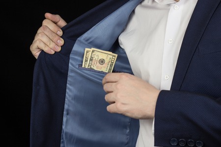 A man in a jacket in a breast pocket holds dollars, a black backgroundの写真素材