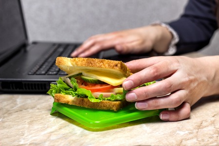 The girl is preparing for dinner at work, pulling out a sandwich, close-upの写真素材