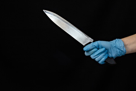 Hand of a girl in a blue medical glove with a knife on a black background, close-upの写真素材