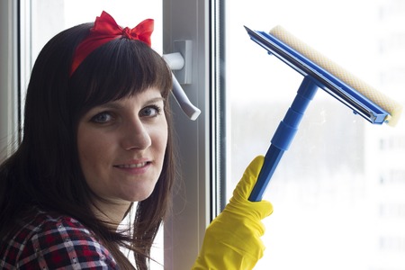 The brunette girl in yellow gloves is washing the windowの写真素材