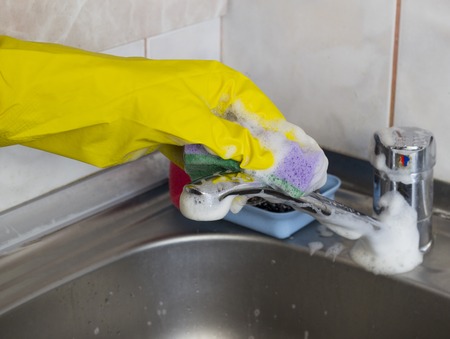 A girl in yellow gloves washes the faucet in the kitchen, close-upの写真素材