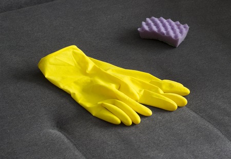 Yellow cleaning gloves and a sponge on the couch, close-upの写真素材