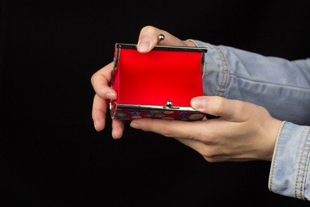 Female hands holding an empty red purse on a black background, close-up