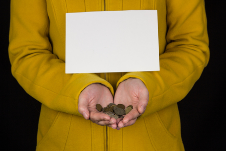 Girl in yellow holds coins in hands and clean sheet for writing, black background, close-up, coins in the palmsの写真素材
