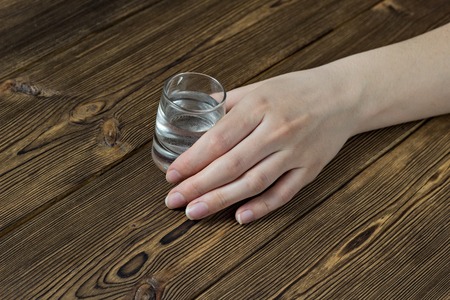 female hand with a glass of alcohol on a wooden table, close-up, female alcoholismの写真素材