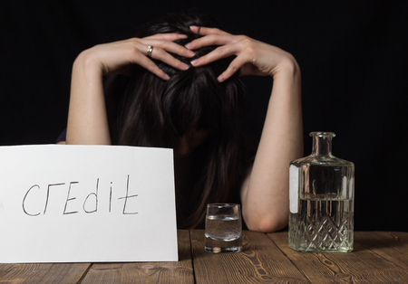 Brunette girl with a glass of vodka and a bottle, inscription on a sheet of credit, problemsの写真素材