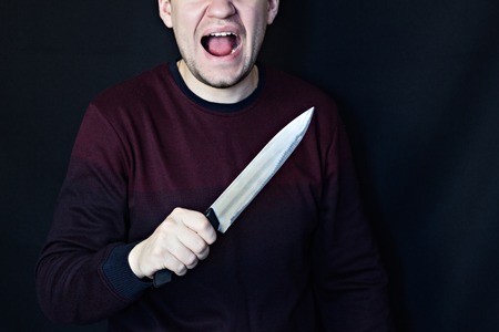 Man with a knife and an open mouth, an attack, a black background, attackの写真素材