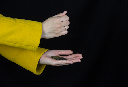 Female hands in a yellow coat pour coins from one hand to another, black background, close-up, moneyの写真素材