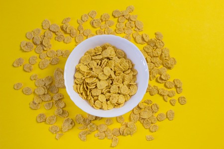 Corn flakes in a plate on a yellow background, nutrition
