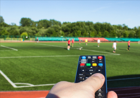 a male hand with a remote control from a TV set against the background of the football field on which they play football, TV remote controlの写真素材