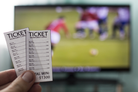 A man's hand holds bookmakers' tickets against the backdrop of a television set running football, Champions Leagueの写真素材