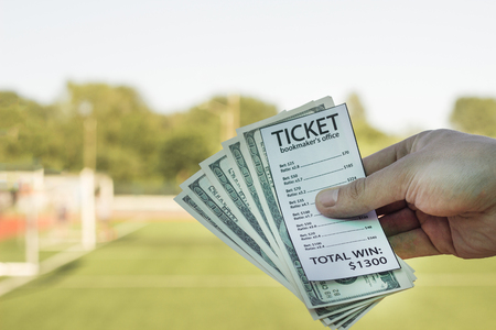 Male hand holding money dollars and bookmaker ticket against the background of a football field, close-up, stadiumの写真素材