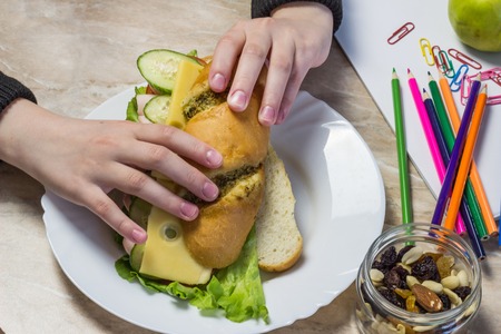 The girl collects a sandwich in school, on a table pencils, paper clips, , juice, dried fruits and textbooks, handsの写真素材