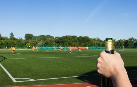 A man opens a bottle of beer on the background of a football field where they play football, close-up, bad habitの写真素材