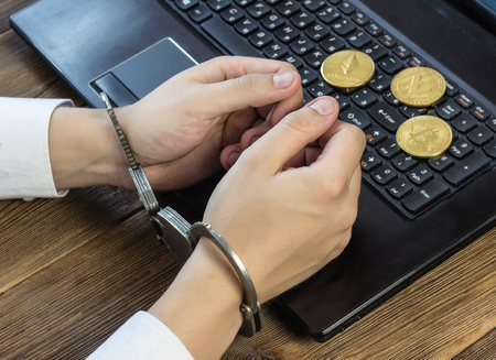 Men's hands in handcuffs at the computer, near lies crypto, mining and hacking, bitcoin and etheriumの写真素材